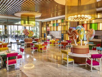 Kolorowa restauracja hotelowa z nowoczesnymi meblami i dużymi oknami.