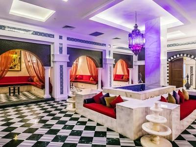 Luksusowy salon hotelowy z dekoracyjnymi niszami do siedzenia, czarno-białą podłogą i fioletowym oświetleniem.