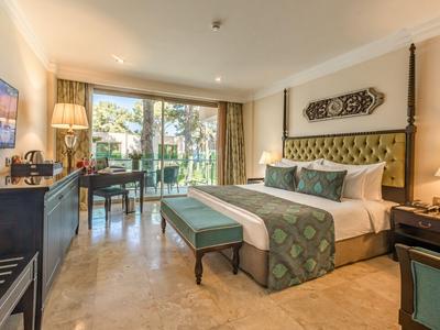 Lichte hotelkamer met groot bed, bureau, tv en uitzicht op de tuin.