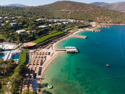 Strandhotelanlage mit Liegestühlen, Stegen und klarem, türkisblauem Wasser an bewaldetem Hang.