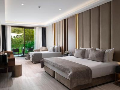 Modernes Hotelzimmer mit zwei großen Betten, grauer Einrichtung und Blick auf eine Terrasse.
