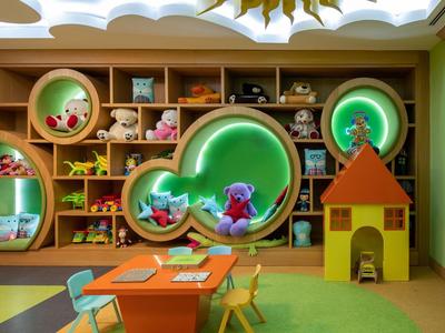 Bunte Kinderspielecke mit Regalen, Plüschtieren und kleinen Tischen in einem Hotel.