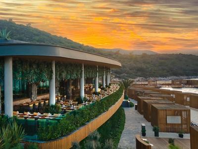 Hotelterrasse mit Abendsonne und Blick auf Hügel und moderne Holzbungalows.