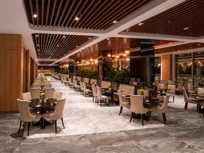 Modern eingerichtetes Hotelrestaurant mit Holzakzenten, grauem Boden und hellen Sitzgruppen.