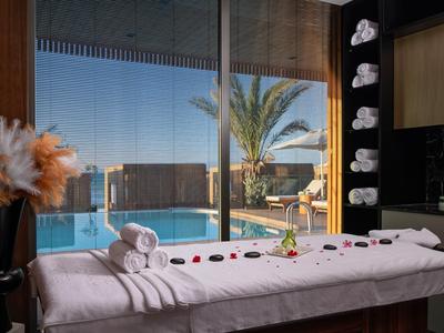 Moderner Wellnessbereich mit Massagebank, Handtüchern und Blick auf Pool und Palmen.