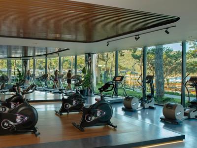 Moderner Fitnessraum mit Fahrrädern und Laufbändern, umgeben von großen Fenstern und Naturblick.