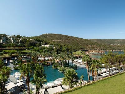 Ein Hotelresort mit Pool, umgeben von Palmen und Hügeln unter klarem Himmel.