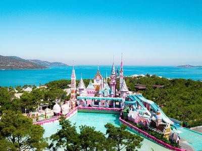 Buntes Schloss und Wasserpark mit Rutschbahnen nahe am Meer in einer grünen Landschaft.