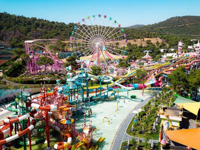 Wasserpark mit Rutschen, Fahrgeschäften und Riesenrad in sonniger Landschaft.