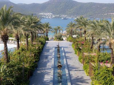 Luxuriöser Hotelgarten mit Palmen, Pool und Blick auf eine Küstenbucht und Berge.