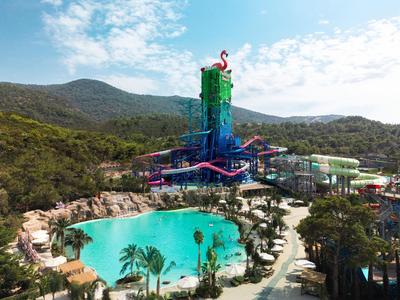 Großer Wasserpark mit Rutschen und Lagune, umgeben von grünen Hügeln und Palmen.