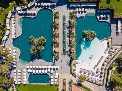 Zwei große Hotelpools mit Liegestühlen und Palmen, von oben aufgenommen.