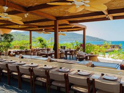 Offenes Restaurant mit Holztisch und Blick auf das Meer und grüne Berge