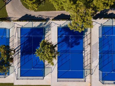 Drei blaue Tennisplätze mit umliegenden grünen Bäumen und Wegen von oben.