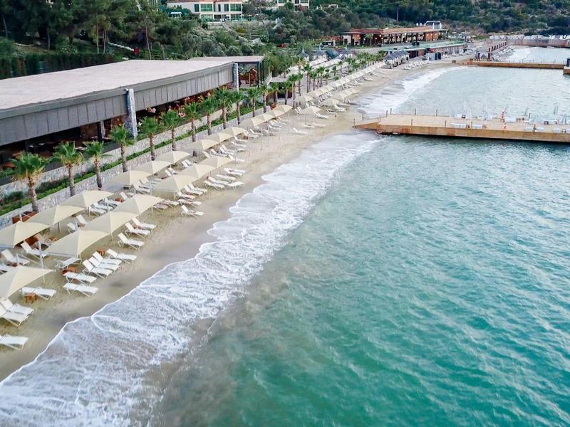 Plaża z leżakami obok długiego molo i spokojnego, turkusowego morza.