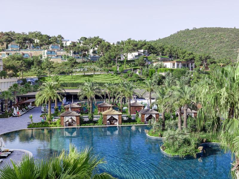 Luksusowy kurort z basenem, leżakami i zielonymi wzgórzami w tle.