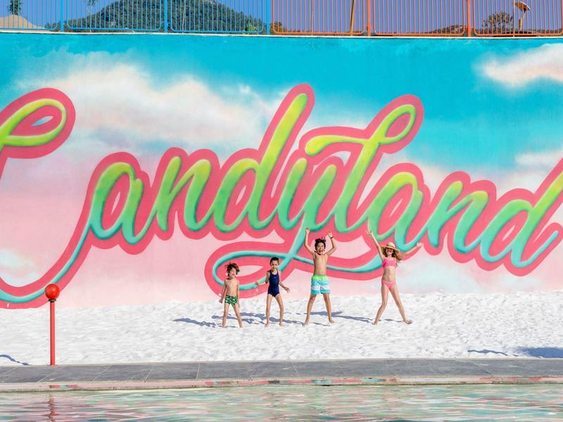 Cztery kobiety spacerują przed kolorową ścianą Candyland na zewnątrz.