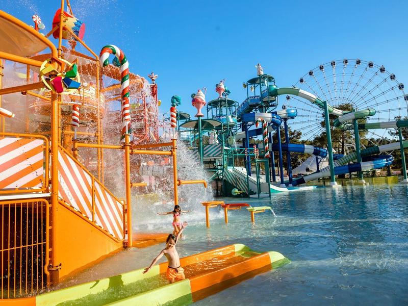 Kolorowy basen w parku wodnym z zjeżdżalniami i dużym diabelskim młynem w tle w słoneczny dzień.