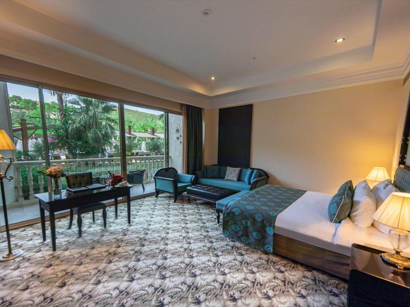 Przestronny pokój hotelowy z dużym łóżkiem, biurkiem, sofą i widokiem na balkon oraz zieleń.