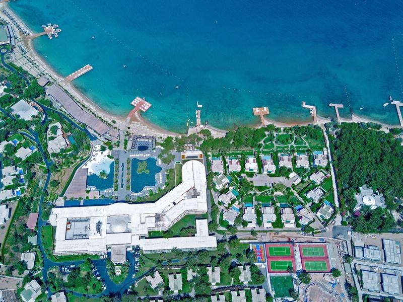 Widok z lotu ptaka na ośrodek z basenem, plażą i wieloma budynkami nad turkusowym morzem.