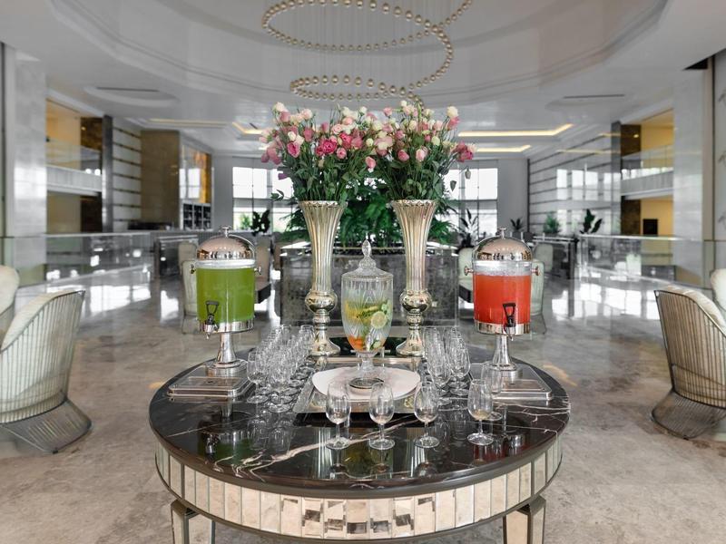 Elegancki salon hotelowy z napojami w szklankach i dekoracją kwiatową na okrągłym marmurowym stole.