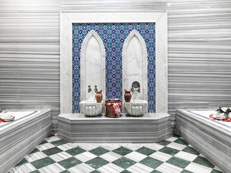 Luksusowy hammam z marmurowymi basenami i niebiesko-białą płytką ścianą.