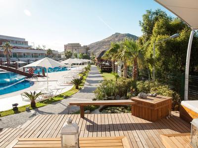 Drewniany taras z jacuzzi, widok na basen i ogród w słonecznym hotelu.