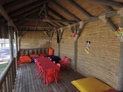 Zadaszony taras z czerwonym stołem i krzesłami, żółtymi poduszkami oraz kolorowymi dekoracjami na ścianie.