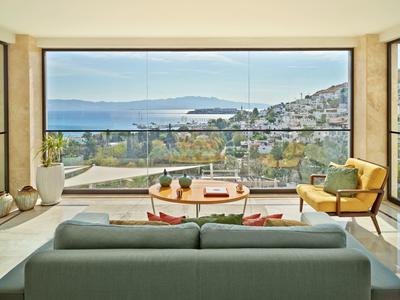 Jasny pokój z sofą, fotelami i dużym oknem z widokiem na morze i nadmorskie miasto.