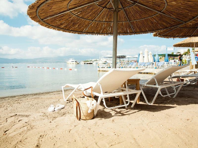 Puste leżaki pod słomianymi parasolami na piaszczystej plaży z widokiem na morze.