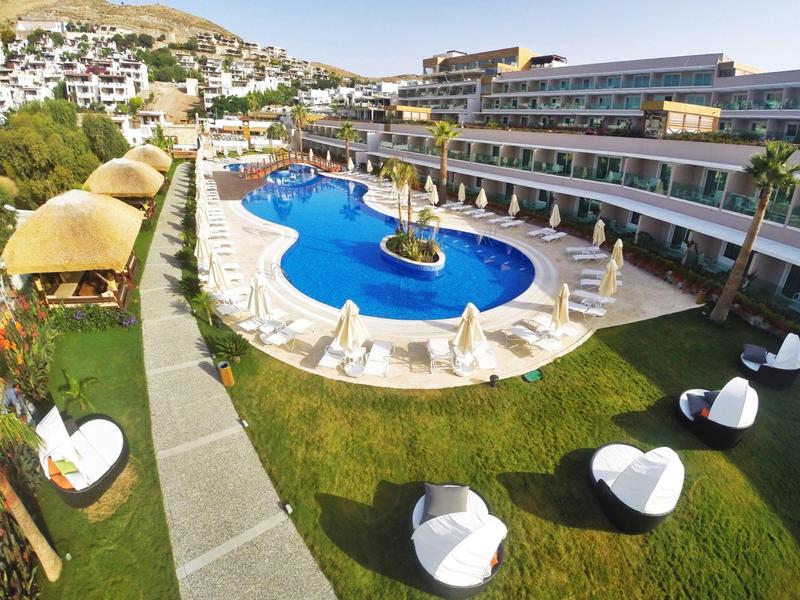 Nowoczesny hotel z okrągłym niebieskim basenem i białymi krzesłami na zielonym trawniku.