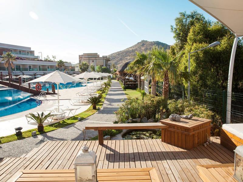 Drewniany taras z jacuzzi, widok na basen i ogród w słonecznym hotelu.