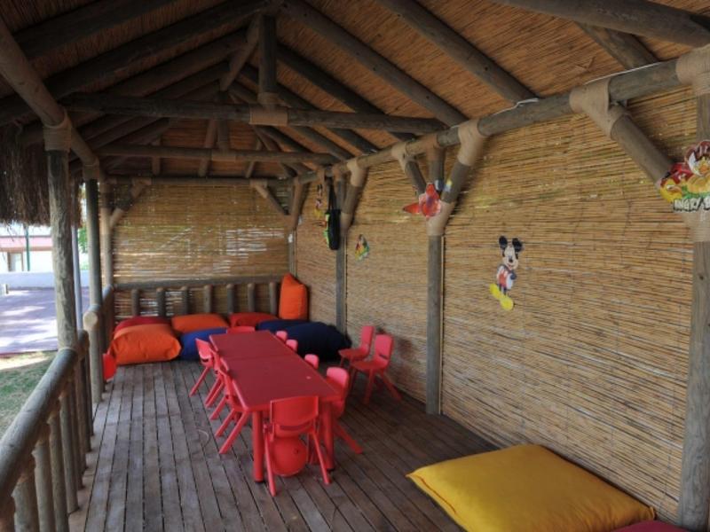 Zadaszony taras z czerwonym stołem i krzesłami, żółtymi poduszkami oraz kolorowymi dekoracjami na ścianie.