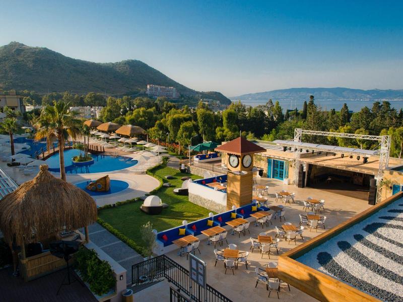 Widok na strefę basenową hotelu z parasolami, leżakami i górami w tle.