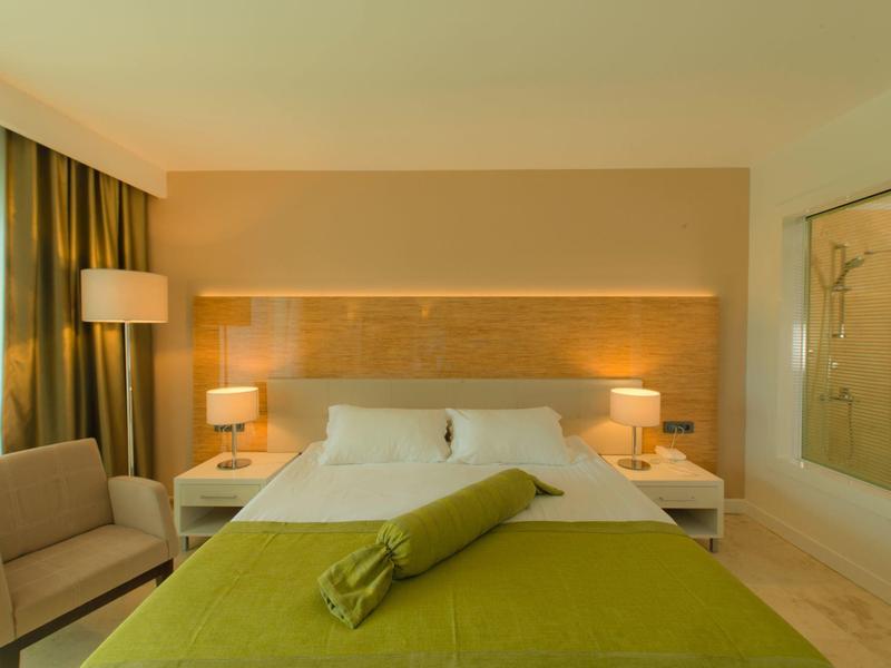 Nowoczesny pokój hotelowy z dużym łóżkiem, zielonym kocem i wygodnym fotelem przy oknie.