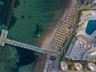 Aerial view of a hotel with pool, beach chairs, and clear sea water.