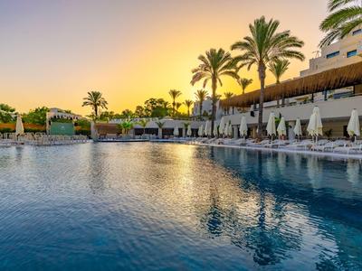 Swimming pool at sunset with sun loungers and palm trees at a resort.