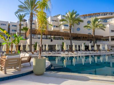 Modern hotel pool with lounge chairs, umbrellas, and palm trees under a clear sky.