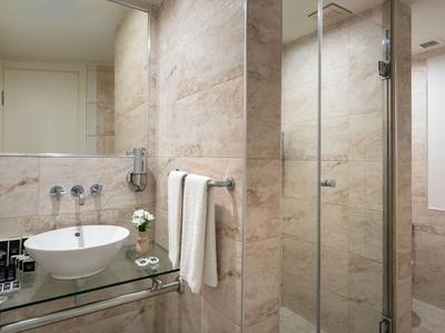 Modernes Badezimmer mit Glasdusche, weißem Waschbecken und Handtüchern in neutralen Tönen.