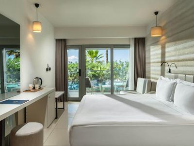 Helles, modernes Hotelzimmer mit großem Bett, Schreibtisch, Terrasse und Blick auf grüne Pflanzen.