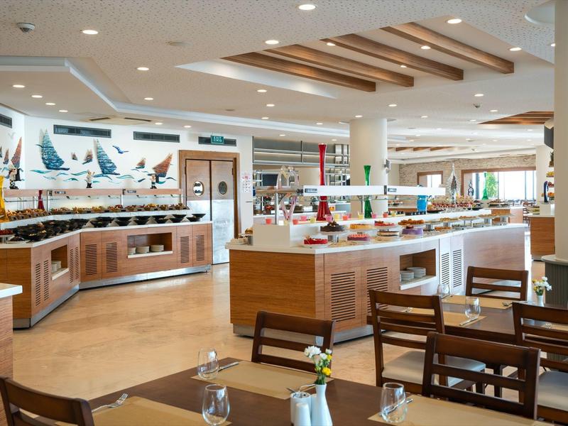 Bright, modern hotel restaurant with buffet and wooden furniture.