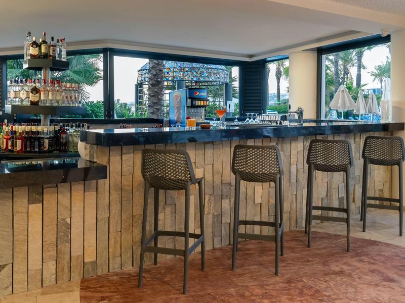 Modern hotel bar with wooden furniture and large glass windows overlooking the terrace.