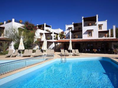 Hotel with outdoor pool, sun loungers, and white umbrellas under clear blue sky.