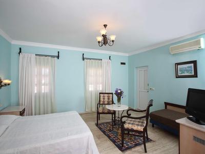 Bright hotel room with two beds, seating area, and TV in a pastel blue space.