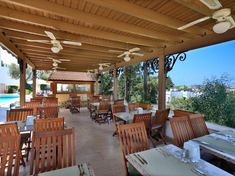 Covered terrace with wooden tables and chairs, overlooking pool and surrounding nature.