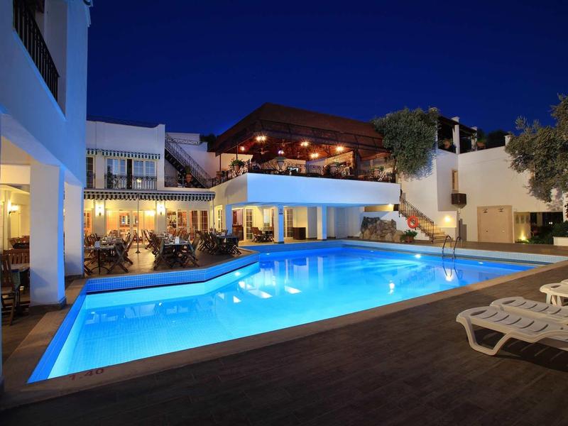Stylishly lit pool area at night with loungers and modern hotel building in the background.