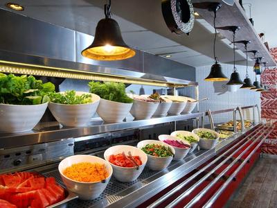 Buffet con varias ensaladas frescas e ingredientes en tazones blancos bajo lámparas colgantes.