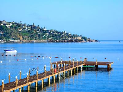 Muelle largo sobre mar tranquilo con barco y paisaje costero al fondo bajo cielo despejado.