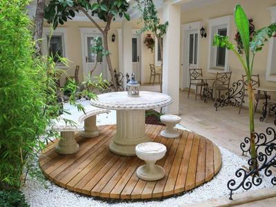 Patio con mesa redonda de piedra, taburetes, plantas y asientos frente a habitaciones de hotel.