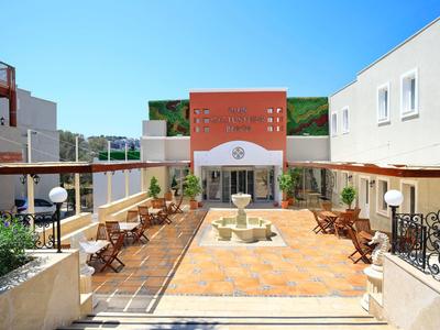 Patio interior iluminado de un hotel con asientos y una fuente central bajo un cielo azul.